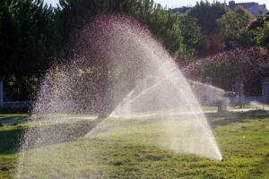 pexels-photo-12887876-12887876 Water sprinkler system spraying lush green grass in a sunny outdoor setting, ideal for lawn care illustrations.
